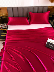 Lustrous mulberry silk flat sheet and two pillowcases in a vibrant fuchsia color, draped on a bed.