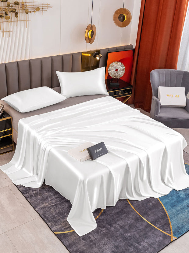 White 19 Momme mulberry silk flat sheet and two pillowcases on a bed, showcasing luxurious sheen.