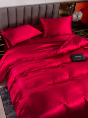 Luxurious red 19 Momme mulberry silk duvet cover set with fitted sheet and two pillowcases on a bed.