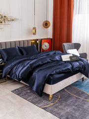 Navy blue 19 Momme mulberry silk duvet cover set with fitted sheet and two pillowcases on a bed.