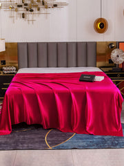 Vibrant fuchsia 19 Momme Mulberry silk seamless flat sheet draped on a bed.