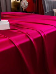Vibrant fuchsia 19Momme mulberry silk seamless flat sheet draped on a bed, showcasing its luxurious sheen.