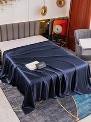 Dark blue 19 Momme Mulberry silk seamless flat sheet draped over a bed, with elegant sheen.
