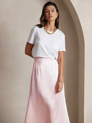 Woman wearing a light pink 19 Momme mulberry silk A-line maxi skirt with a white t-shirt and gold jewelry.