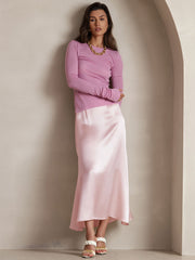 Woman in a light pink mulberry silk A-line maxi skirt with a subtle sheen, paired with a long-sleeve top.