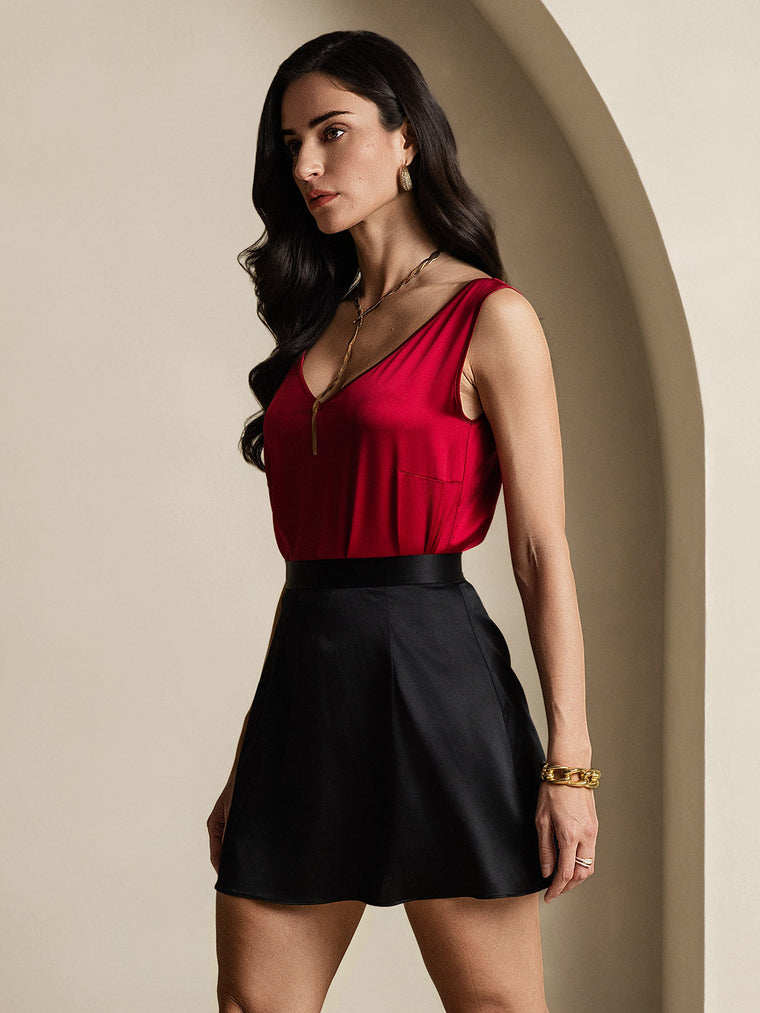 Woman in a red mulberry silk top and black A-line mini skirt with a zipper design.