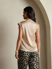 Woman wearing a champagne 19Momme silk cap sleeve cowl neck top and leopard print pants.