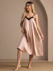 Blonde woman in a blush pink 19Momme mulberry silk midi nightgown with black contrast V-neck and spaghetti straps.