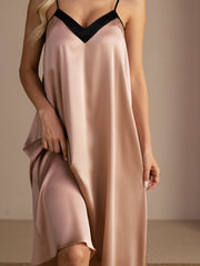 Blonde woman in a blush pink mulberry silk midi nightgown with black V-neck and spaghetti straps.