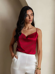 Woman wearing a red 19Momme mulberry silk cowl neck camisole top with white pants.