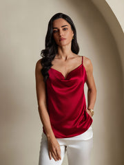 Woman wearing a red mulberry silk cowl neck camisole top with white pants.