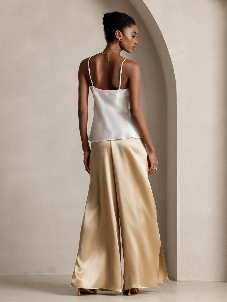 Woman in white mulberry silk top and gold flowy high-slit palazzo pants.