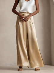 Women's fashionable gold mulberry silk palazzo pants with high slits, paired with a white silk top.