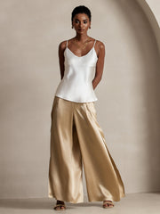 Woman in white mulberry silk camisole and fashionable flowy high-slit gold palazzo pants.