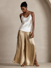 Woman in fashionable flowy high-slit mulberry silk palazzo pants and a white silk camisole.