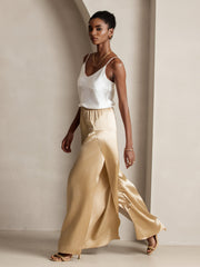 Woman in fashionable gold mulberry silk high-slit palazzo pants and white silk top.
