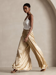 Woman in fashionable flowy high-slit palazzo pants made of golden mulberry silk, paired with a white silk top.