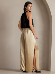 Woman wearing fashionable flowy high-slit palazzo pants in gold 19 Momme mulberry silk with a black silk top.