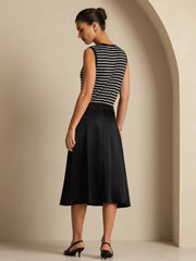 Woman in black mulberry silk high-waist A-line midi skirt with pockets, paired with a striped top.