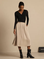 Woman in a beige 19Momme silk high-waist A-line pleated midi skirt with pockets and a black top.
