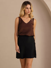 Woman in a brown V-neck silk top and black high-waist short skirt.