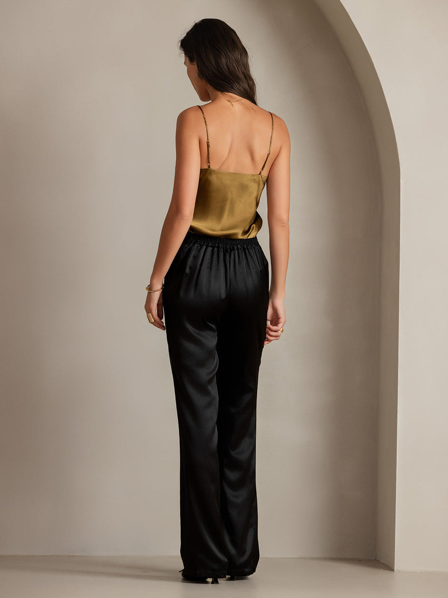 Woman in black 19Momme mulberry silk high waist straight fit pants with back elastic waist and a gold silk camisole.