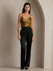 Woman in black 19Momme silk high waist straight fit pants with gold buttons and a gold silk camisole.