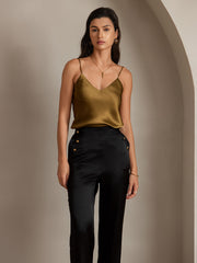 Woman in a gold silk camisole and black high-waist straight-fit silk pants with gold button details.