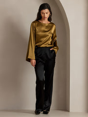 Woman in a gold mulberry silk top and black high-waist straight-fit silk pants with button details.