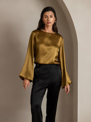 Woman in olive green mulberry silk top with bell sleeves and black high-waist straight-fit pants.
