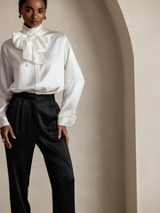 Woman in white 19Momme silk blouse with bow and black high-waist straight-fit silk pants with side pockets.