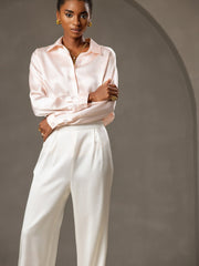 Woman in a light pink mulberry silk shirt and white high-waist wide-leg pleated silk pants.