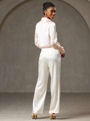 Smiling woman in a light pink silk blouse and white 19Momme silk high waist wide leg pleated pants.