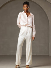 Woman wearing a light pink mulberry silk blouse and white 19Momme silk high waist wide leg pleated pants.