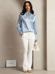 Light blue 19Momme mulberry silk keyhole neck blouse with pearl buttons, worn with white pants.