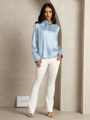 Light blue mulberry silk keyhole neck blouse with pearl buttons, worn by a woman with white pants.