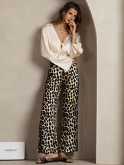 Woman in 19Momme silk leopard print straight leg pants with side pockets and a cream silk top.
