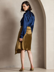 Woman in a navy mulberry silk long sleeve high neck bow tie blouse and a gold satin skirt.