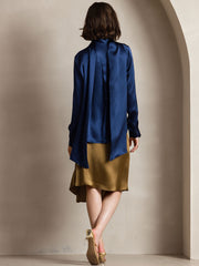 Women's navy mulberry silk long sleeve high neck bow tie blouse with a flowing back over a gold skirt.