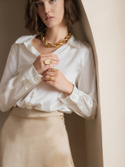 Woman wearing a white 19Momme silk long sleeve lapel collar shirt with a gold skirt and jewelry.