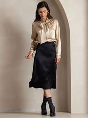 Gold 19Momme mulberry silk long sleeve tie neck blouse with a black midi skirt.