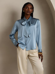 Women's 19Momme Mulberry silk long sleeve tie neck blouse in light blue, paired with cream pants.