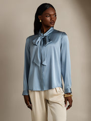 Women's mulberry silk long sleeve tie neck blouse in light blue, paired with cream pants.
