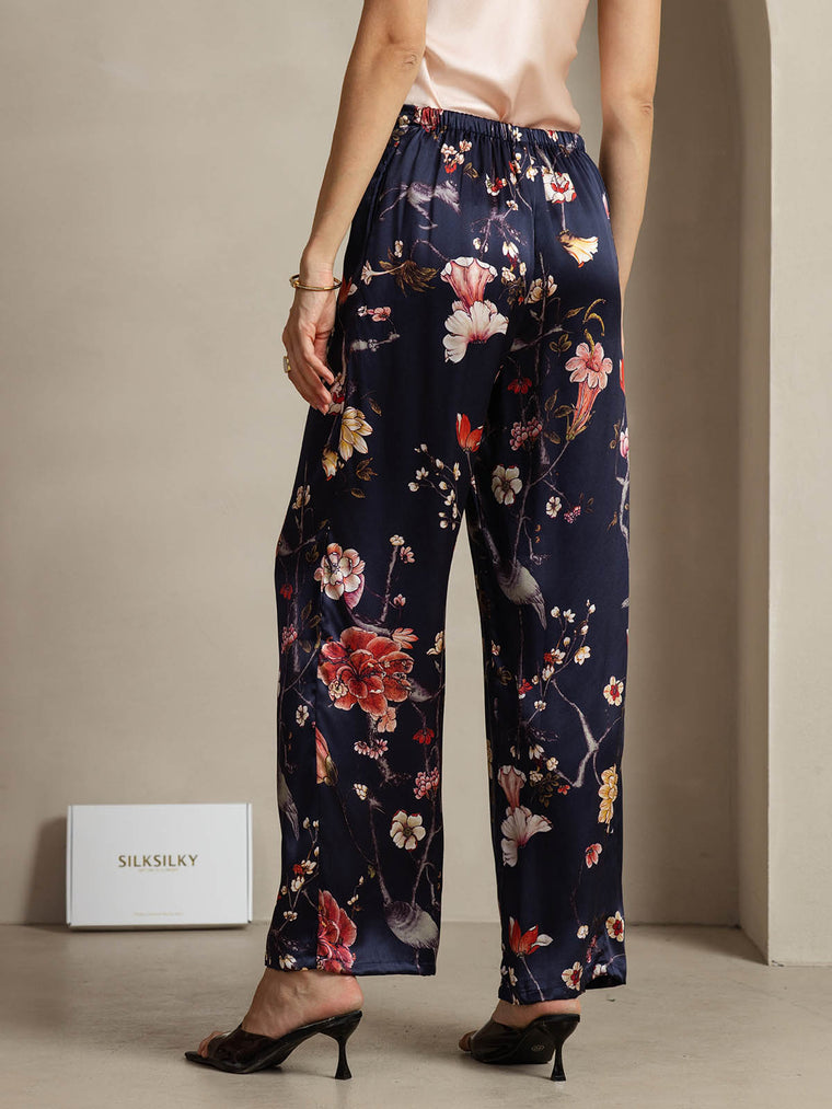 Women's navy mulberry silk wide-leg pants with a vibrant floral and bird print, featuring side pockets.