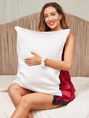 Woman in red silk nightgown holding a white 19 Momme mulberry silk pillowcase and scrunchie set.