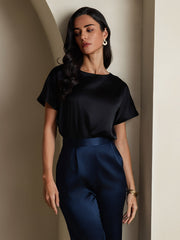 Woman wearing a black 19 Momme mulberry silk boat neck short sleeve t-shirt with navy silk pants.