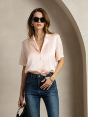 Women's light pink mulberry silk short-sleeve notched lapel shirt with button-up design, paired with jeans.