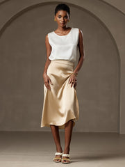 Woman wearing a white 19Momme mulberry silk sleeveless round neck tank top and a gold silk midi skirt.