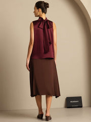 Women's mulberry silk sleeveless tie-neck blouse in maroon, paired with a brown skirt.