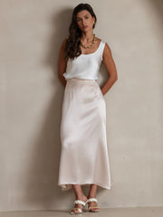 White 19Momme mulberry silk sleeveless U-neck tank top on a woman, paired with a light pink silk skirt.
